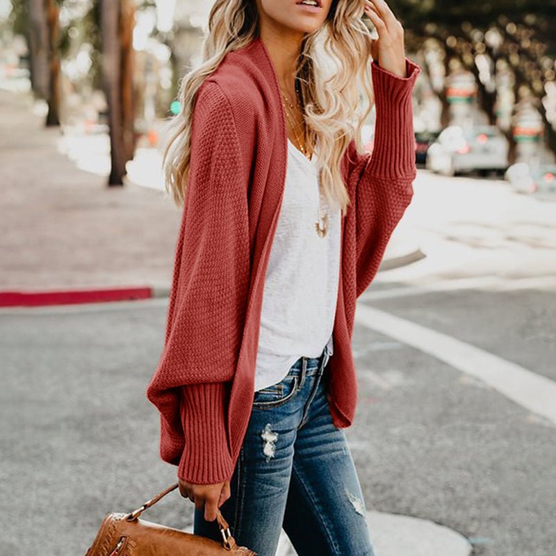 Frau in rotem Strickcardigan, weiße Bluse, Jeans, braune Tasche, Straße im Hintergrund.