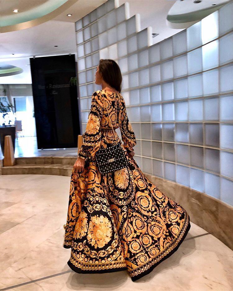 Frau in langem, gemustertem Kleid mit Tasche, modernes Interieur, elegantes Design.