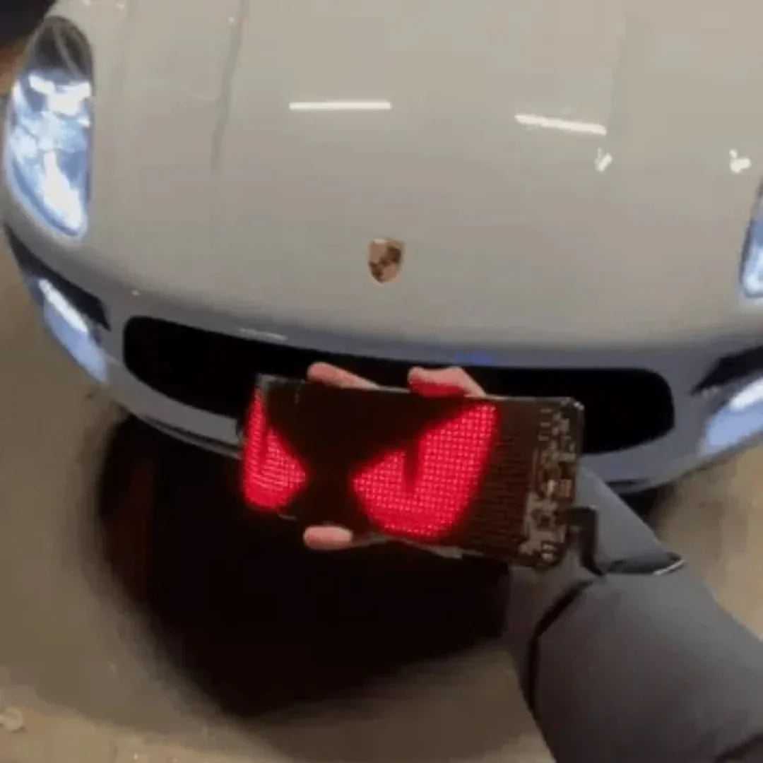 Hand hält LED-Display mit roten Augen vor weißem Porsche, Autozubehör, Beleuchtung.