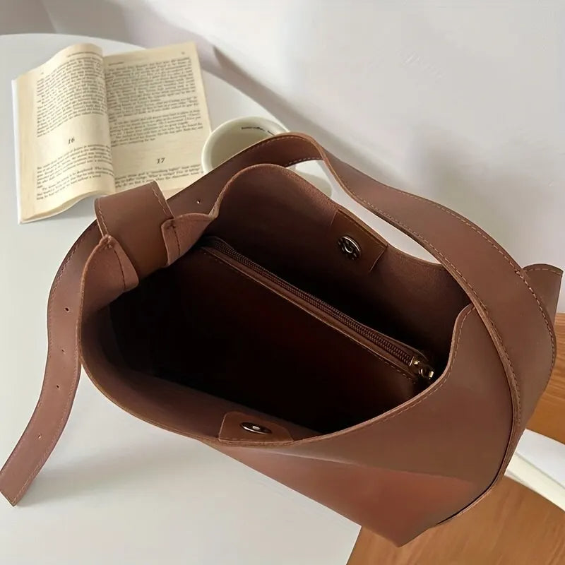 Braune Ledertasche mit offenem Hauptfach, Innenfach mit Reißverschluss, auf weißem Tisch.