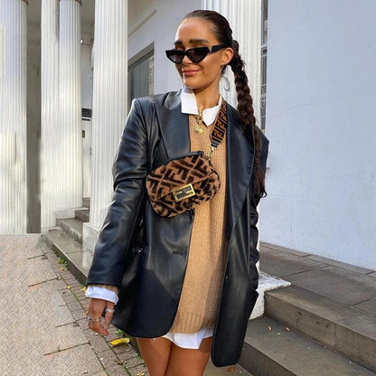 Frau in schwarzer Lederjacke, braunem Pullover, Sonnenbrille, mit gemusterter Umhängetasche.