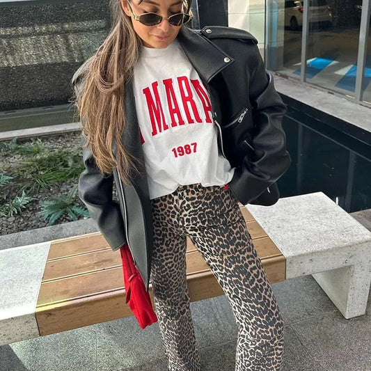 Frau in schwarzer Lederjacke, weißem T-Shirt und Leopardenhose, modischer Streetstyle-Look.