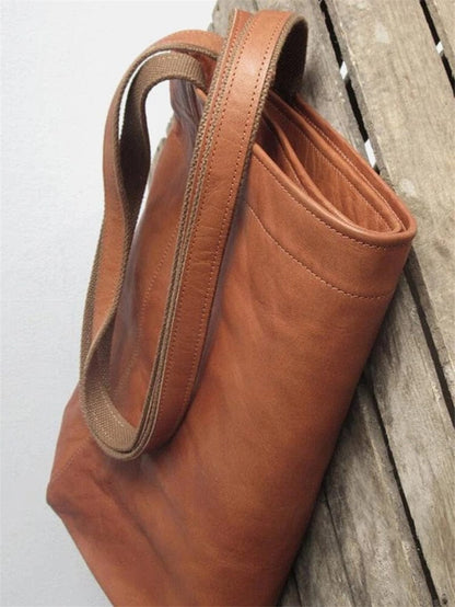 Braune Ledertasche mit robusten Trägern auf Holzhintergrund, langlebige Tragetasche.