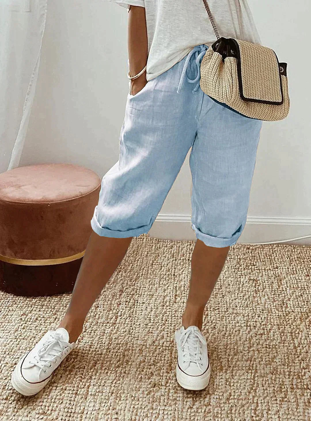 Damen Leinenhose in Hellblau, lässig, mit Kordelzug, kombiniert mit weißen Sneakers und Strohtasche.