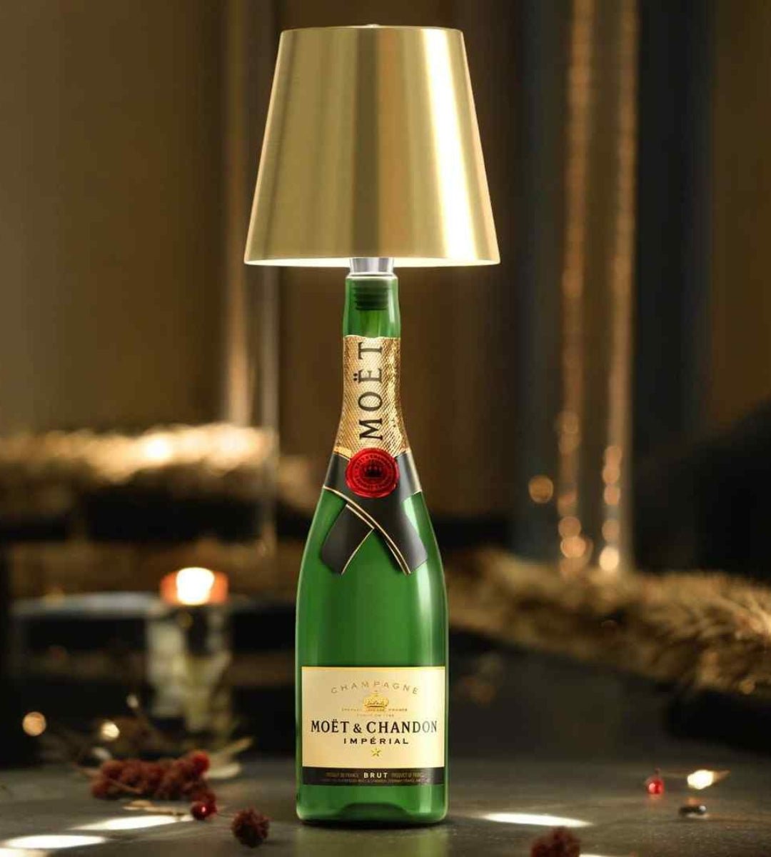 Lampa med guldfärgad metallskärm på en grön champagneflaska, stämningsfullt placerad bland juldekorationer och levande ljus. 1