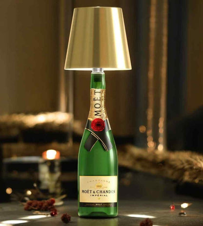 Lampa med guldfärgad metallskärm på en grön champagneflaska, stämningsfullt placerad bland juldekorationer och levande ljus. 1