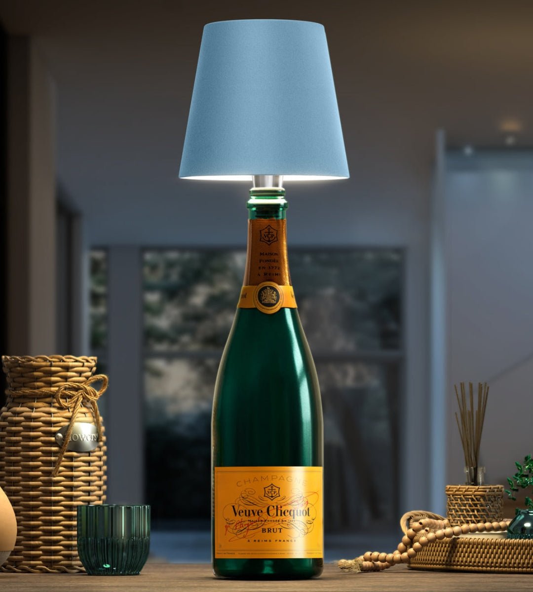 Lampa med ljusblå skärm på en grön champagneflaska, omgiven av flätade korgar och pärlor på ett träbord. 6
