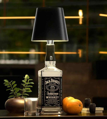 Lampa med svart skärm på en fyrkantig glasflaska, stylad med apelsiner, en kruka med växt och ett glas. 2