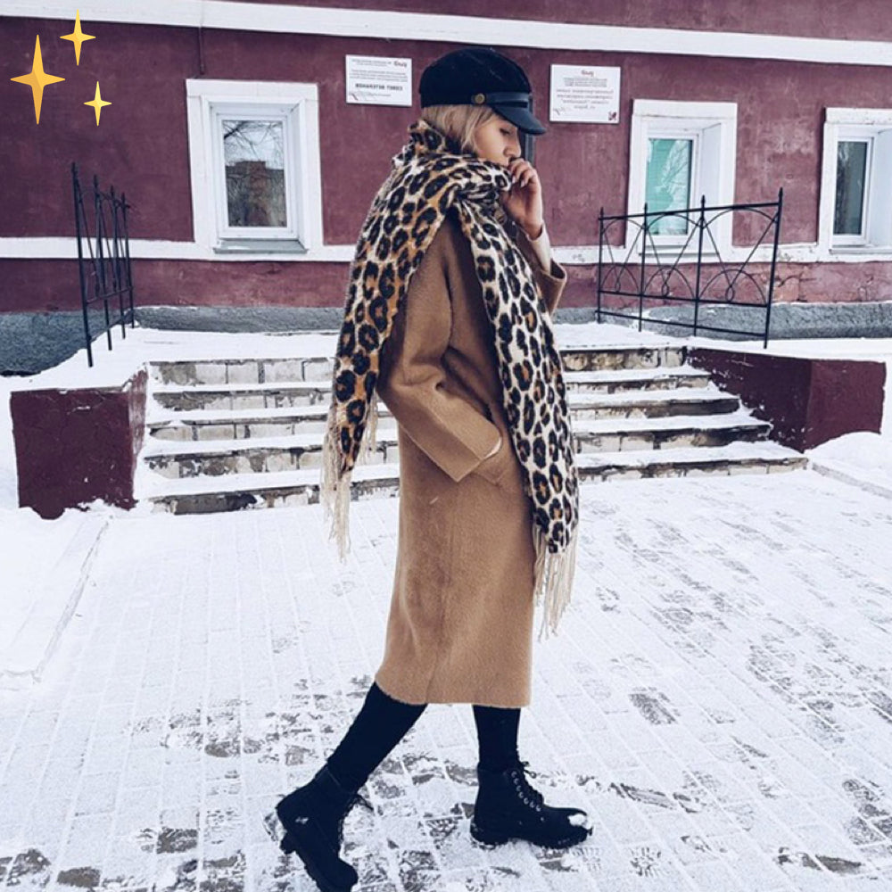 Frau im Wintermantel mit Leoparden-Schal, schwarze Stiefel, schneebedeckter Gehweg.