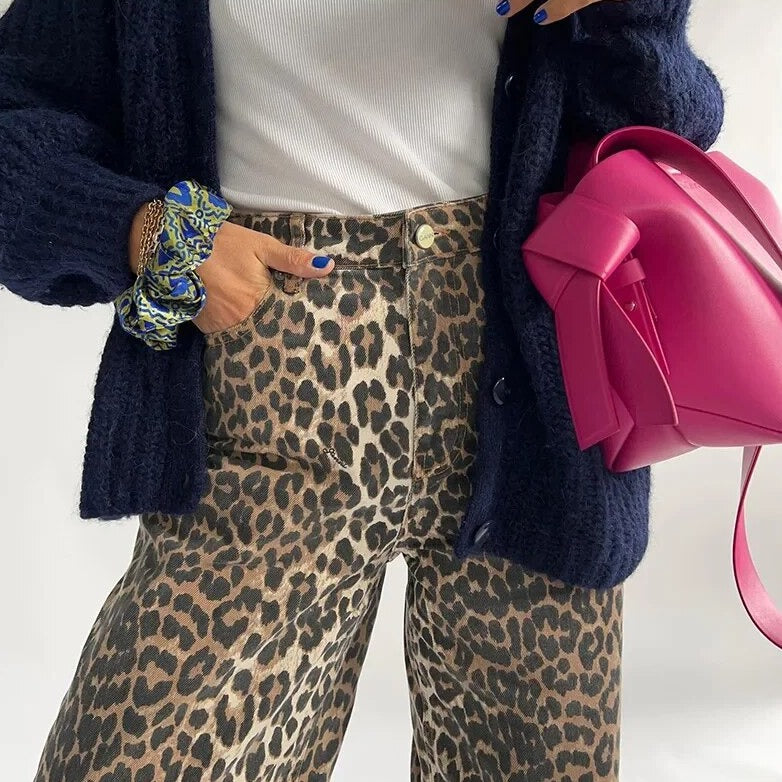 Frau in Leopardenhose, weißem Top, schwarzer Strickjacke, pinke Tasche, modisch, trendy.