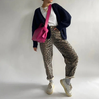 Frau in Leopardenhose, weißem T-Shirt, schwarzer Strickjacke, pinker Tasche, weißen Sneakers.