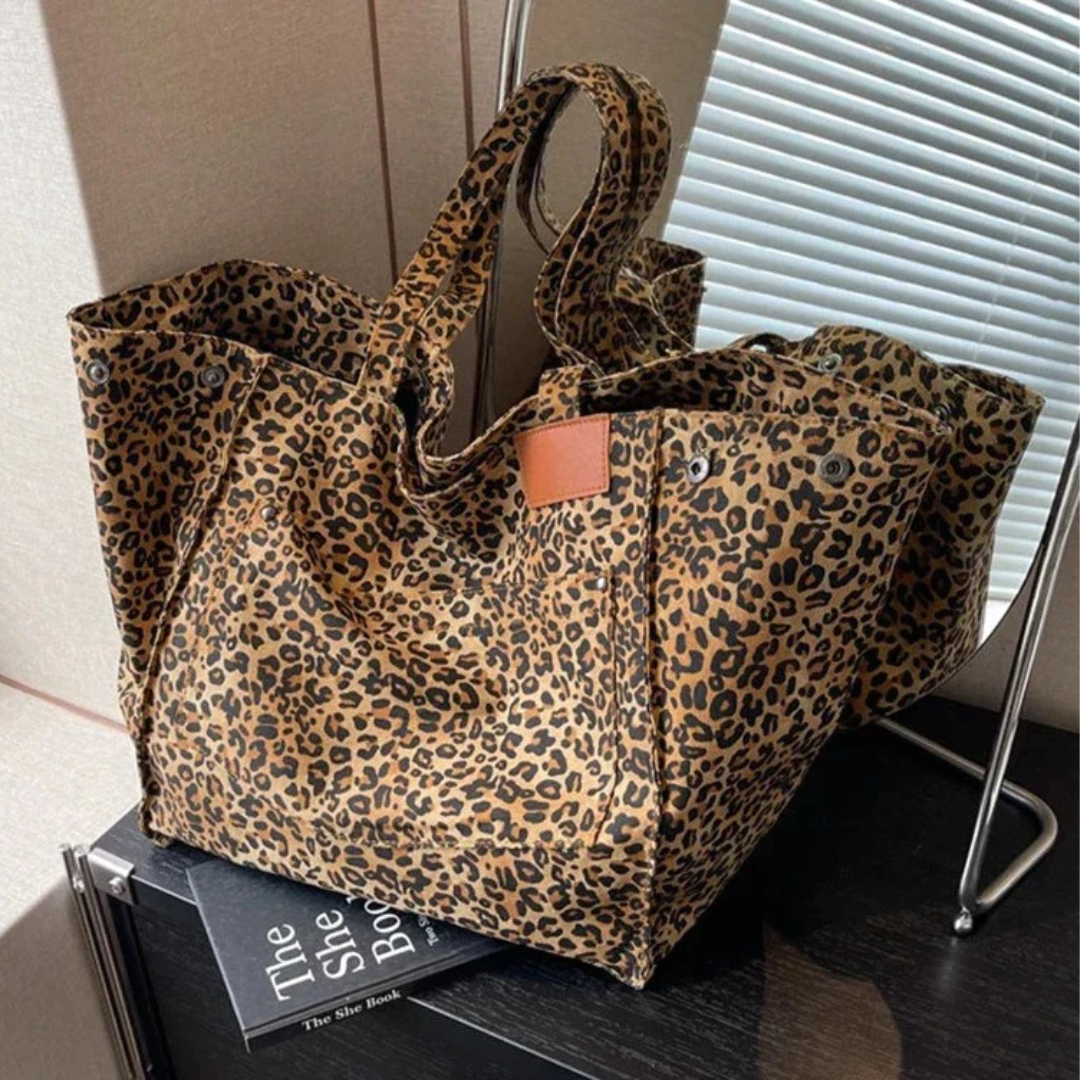 Leopardenmuster Einkaufstasche aus Stoff, braun-schwarz, auf Tisch neben Buch und Lampe.