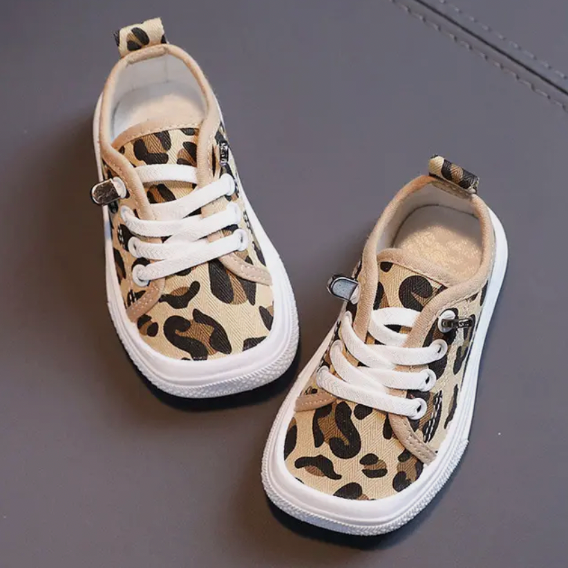 Leopardenmuster-Kinderschuhe, beige, mit weißen Schnürsenkeln, auf grauem Hintergrund.