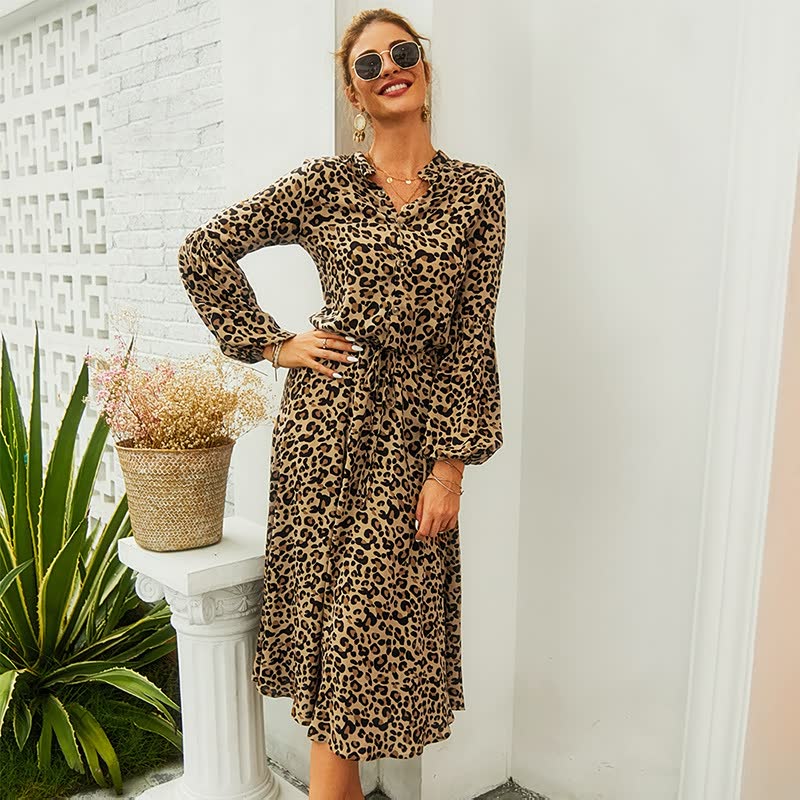 Frau in langem, gepunktetem Leopardenkleid, Sonnenbrille, lächelnd, draußen stehend.