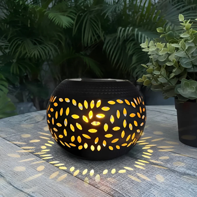 Schwarze Solarleuchte mit Blattmuster, beleuchtet, auf Holztisch im Garten, dekorative Beleuchtung.