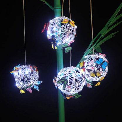 Leuchtende LED-Kugeln mit Schmetterlingen, dekorative Gartenbeleuchtung, Nachtaufnahme.