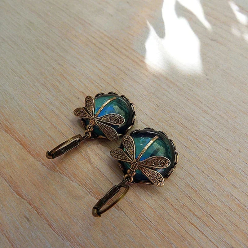 Vintage bronzene Libellen-Ohrringe, goldfarben, modisch, für Damen, auf Holzoberfläche.
