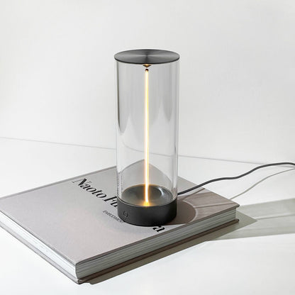 Moderne Tischlampe aus Glas und Metall, zylindrisch, auf Buch, minimalistisches Design.