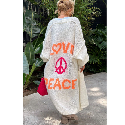 Frau im weißen Strickmantel mit "Love Peace" Aufdruck, roter Tasche, draußen.