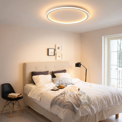 Ringlampa i taket i ett sovrum med bäddad säng, golvlampa, tavlor och en svart stol med bok. 9