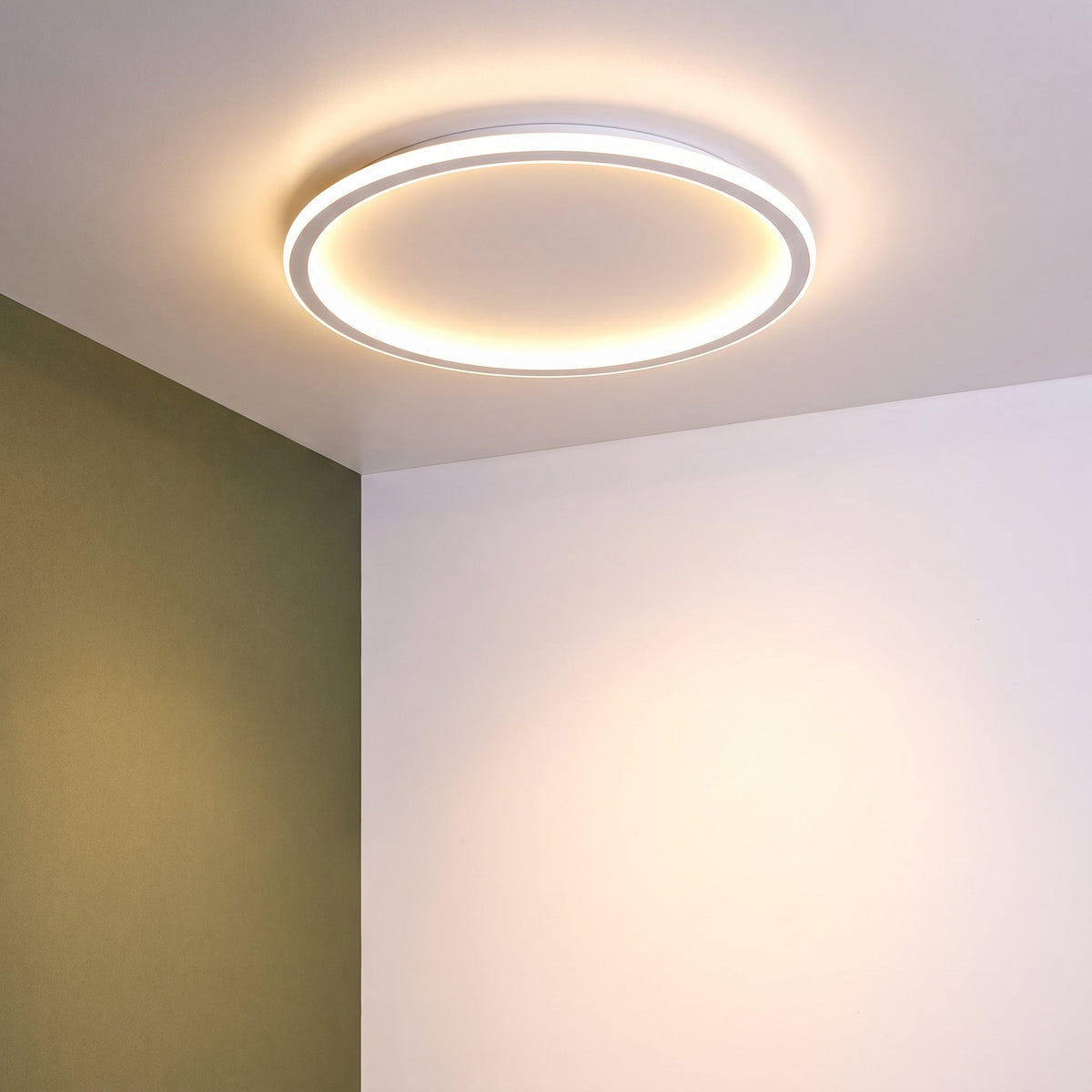 Tänd vit ringlampa i taket intill ett takhörn, med en olivgrön vägg till vänster. 10