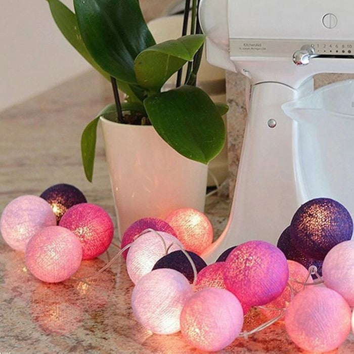 Lichterkette mit bunten Kugeln, rosa und lila, auf Küchentheke neben Pflanze und Mixer.