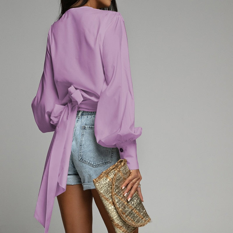 Frau in lila Bluse und Jeansshorts mit goldener Clutch, modisch, elegant, Freizeitkleidung.