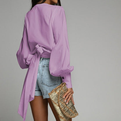 Frau in lila Bluse und Jeansshorts mit goldener Clutch, modisch, elegant, Freizeitkleidung.