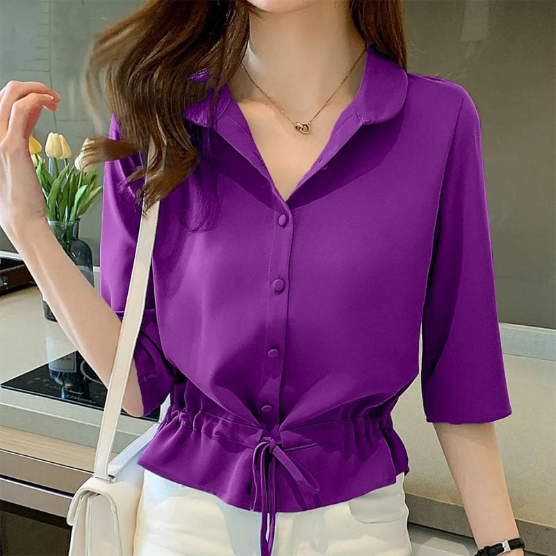 Frau in lila Bluse mit Kordelzug, 3/4-Ärmeln, weiße Hose, moderne Mode, Innenraum.