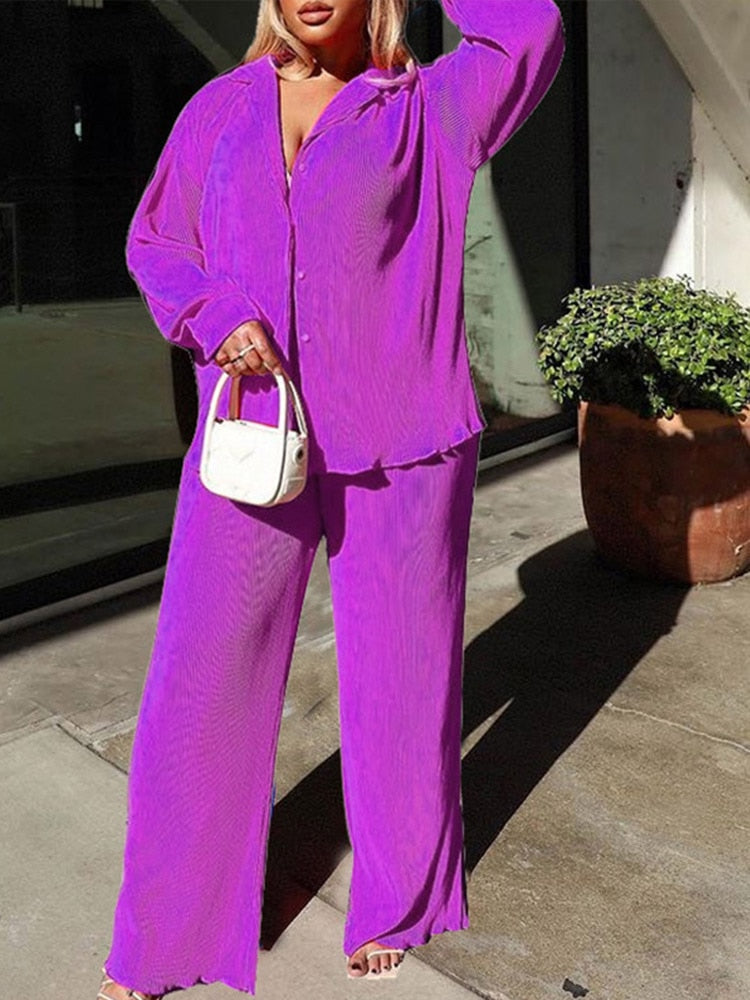Frau in lila Oversize-Anzug mit weißer Handtasche, modisch, urbaner Stil.