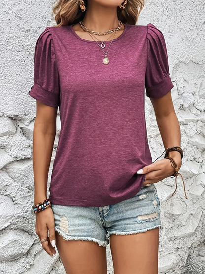 Frau in lila T-Shirt mit Puffärmeln und Jeansshorts vor weißer Wand.