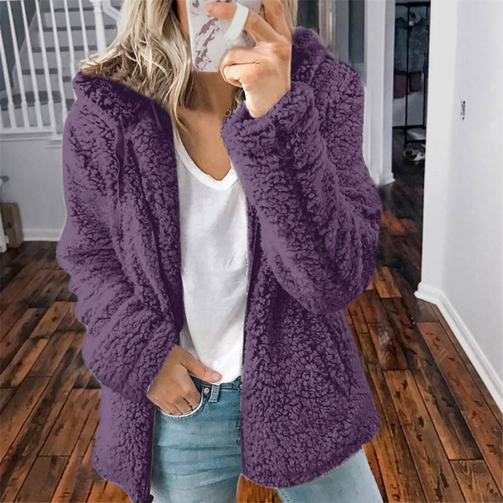 Frau in lila Teddyfelljacke, weißem T-Shirt, Jeans; gemütliche Wintermode, Innenraum.