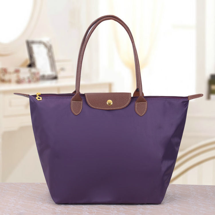 Lila Handtasche aus Nylon mit braunen Ledergriffen auf einem Tisch im eleganten Raum.