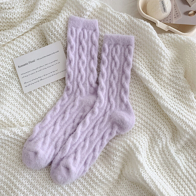 Lila Wollsocken mit Zopfmuster auf weißem Strickhintergrund, gemütliche Wintermode.