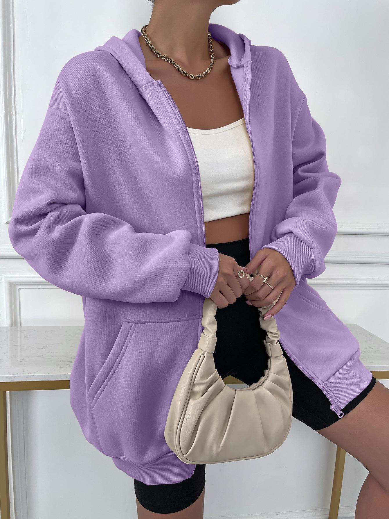 Frau in lila Kapuzenpullover, weißem Top, schwarzer Shorts, beige Handtasche, modisch, lässig.