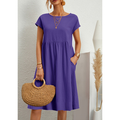 Frau in lila Baumwollkleid mit kurzen Ärmeln, hält eine Strohtasche, Boho-Stil.