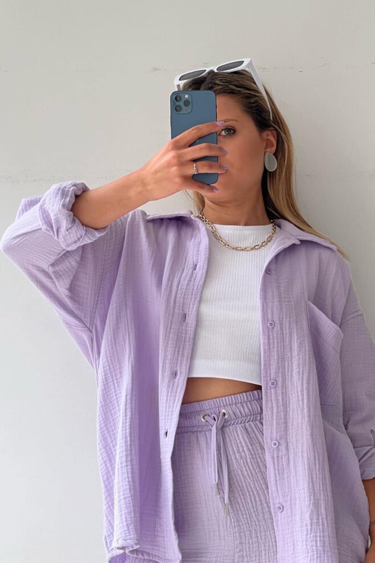 Frau in lila Langarmhemd und Shorts-Set, weißes Top, Smartphone, Sonnenbrille, modisch.