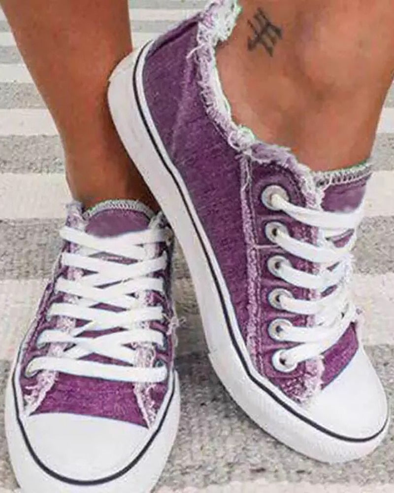 Lila Damen-Sneaker aus Canvas mit weißen Schnürsenkeln, lässiger Stil, auf gestreiftem Teppich.