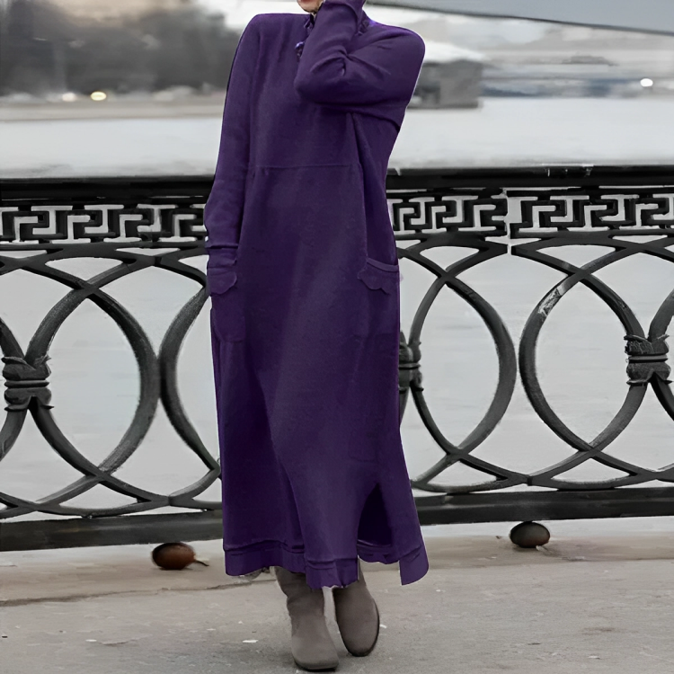 Frau in langem, lila Strickkleid und Stiefeln auf Brücke im Freien.