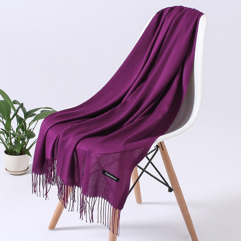 Lila Kaschmirschal auf weißem Stuhl, weiches Material, modisches Accessoire, Pflanze im Hintergrund.