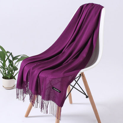 Lila Kaschmirschal auf weißem Stuhl, weiches Material, modisches Accessoire, Pflanze im Hintergrund.