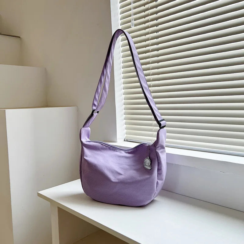 Lila Umhängetasche aus Stoff, modern, minimalistisch, Damenmode, Fensterbank, Tageslicht.