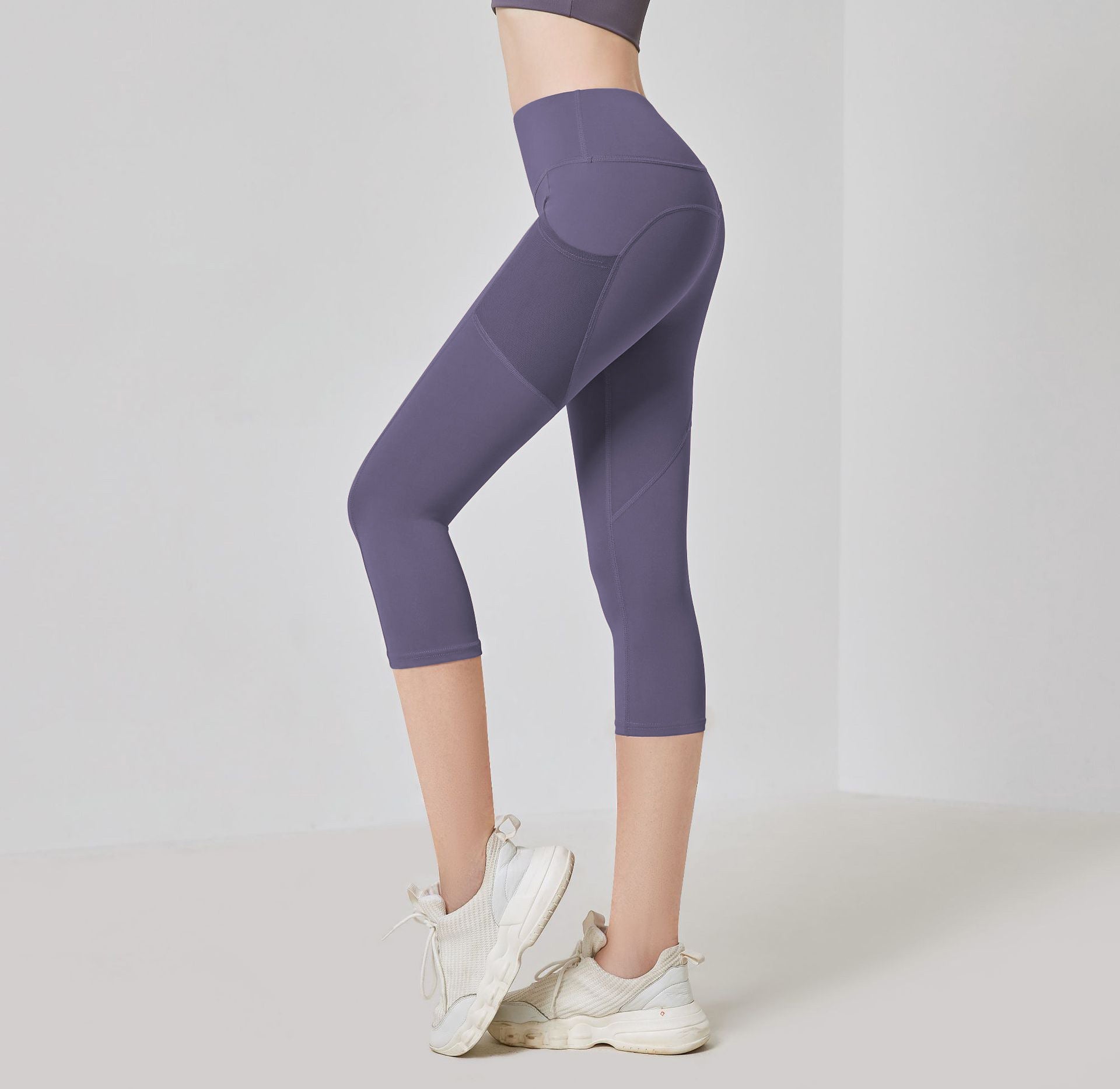 Frau in lila Sportleggings, knielang, mit weißen Turnschuhen, Fitnessmode, seitliche Ansicht.