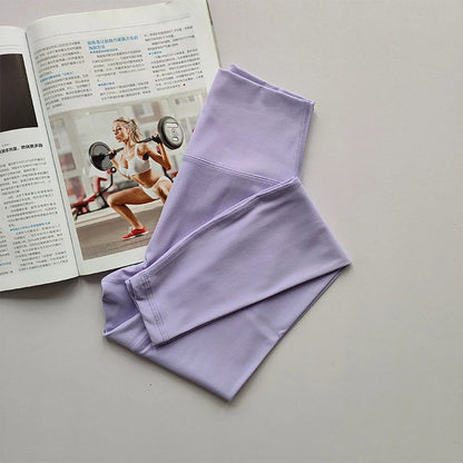 Lila Sportleggings aus Stretchmaterial neben Fitnessmagazin auf grauem Hintergrund.