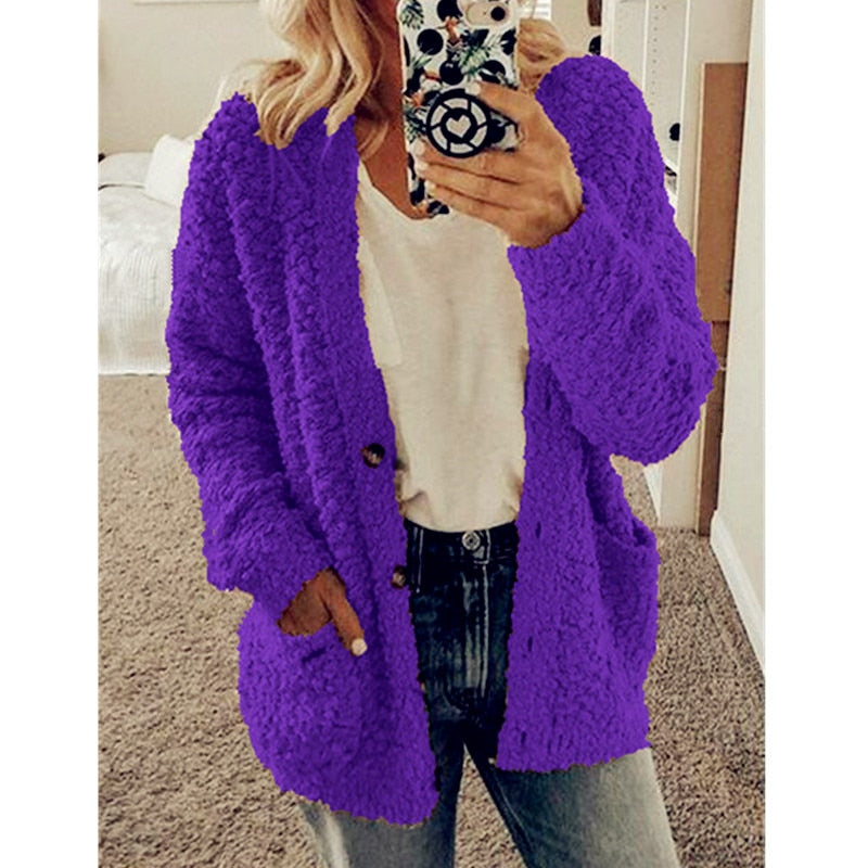 Frau in lila Strickjacke, weißem T-Shirt, Jeans, Smartphone mit gemustertem Case.