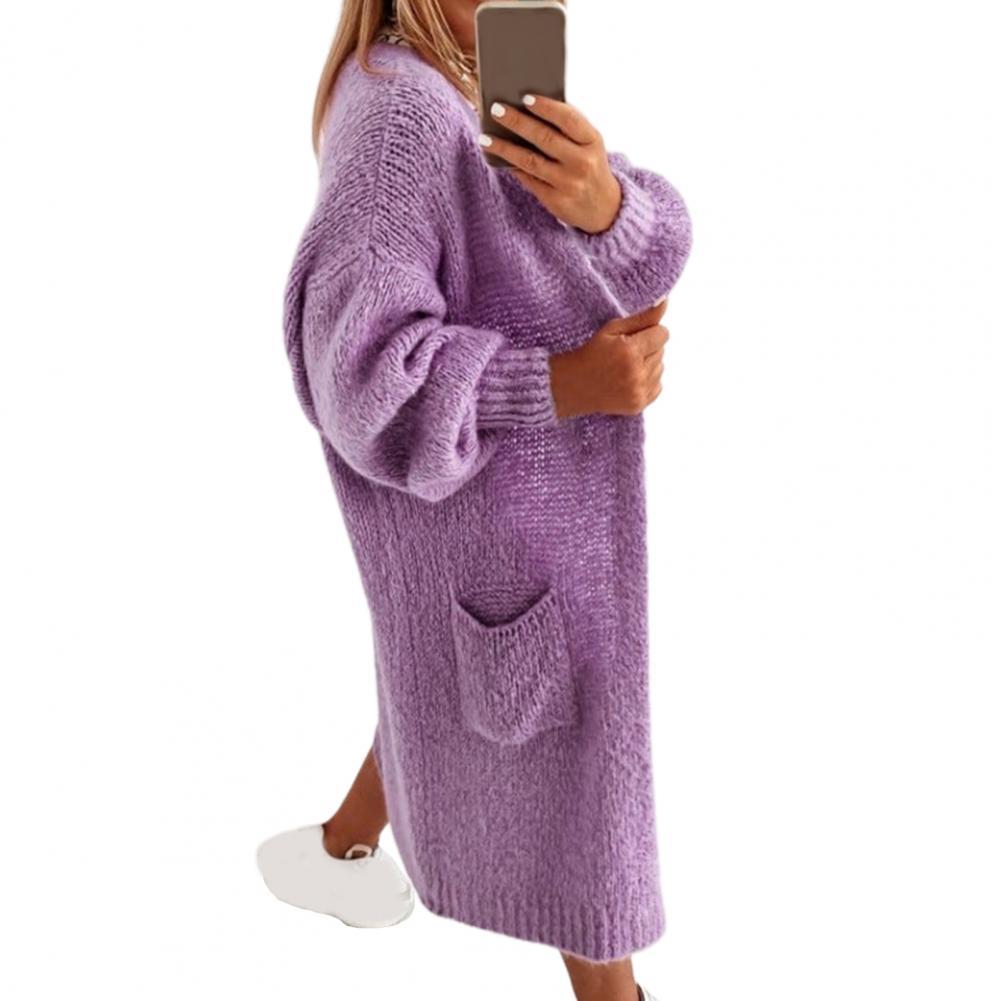 Frau in lila Strickcardigan mit Taschen, Smartphone in der Hand, weiße Sneaker.