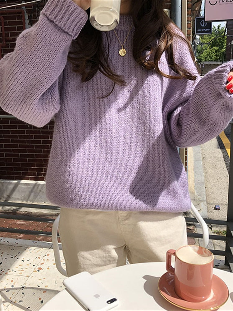 Frau in lila Strickpullover trinkt Kaffee, sitzt draußen, Smartphone und Tasse auf Tisch.