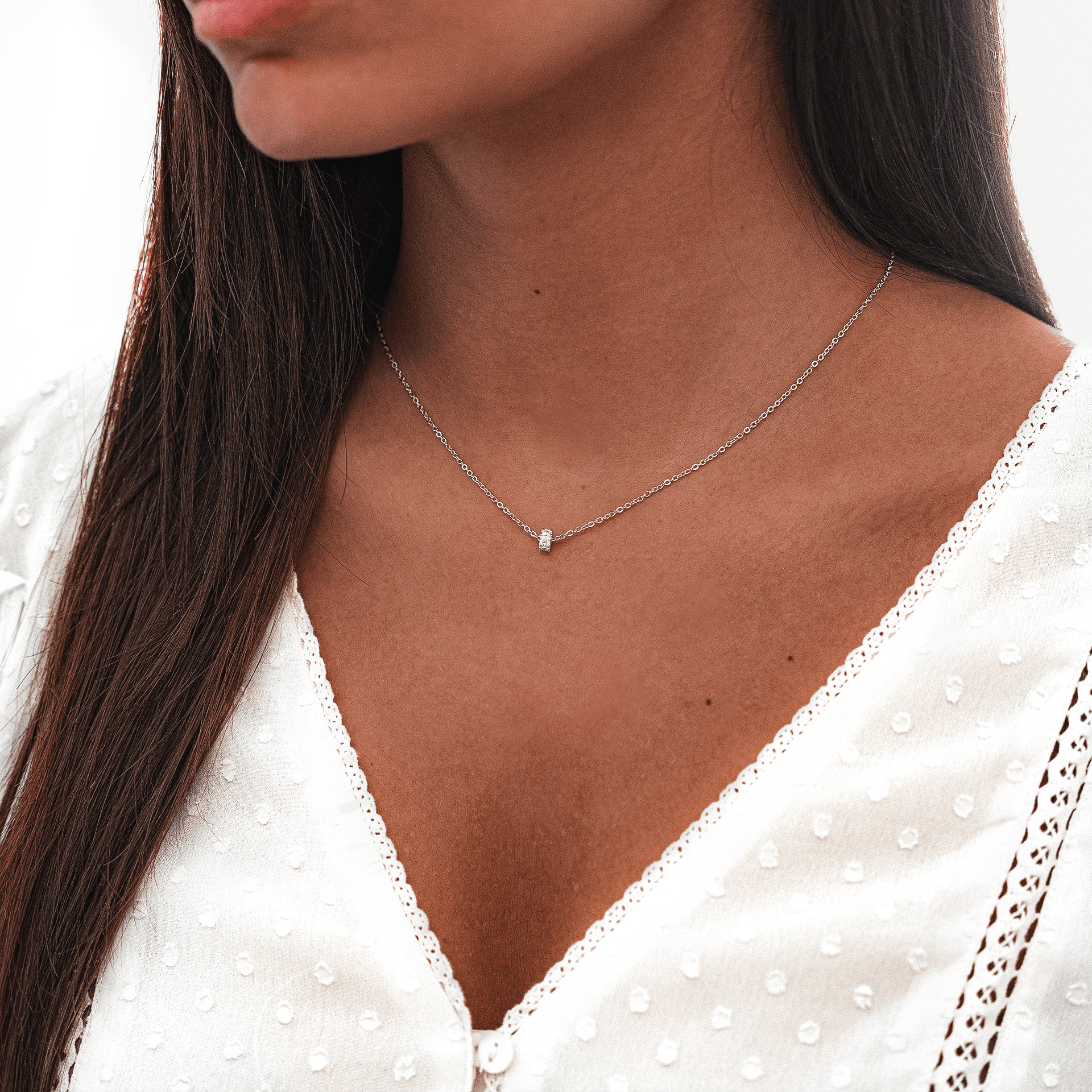 Frau mit silberner Halskette, schlichtes Design, eleganter Schmuck, weißes Spitzenkleid.