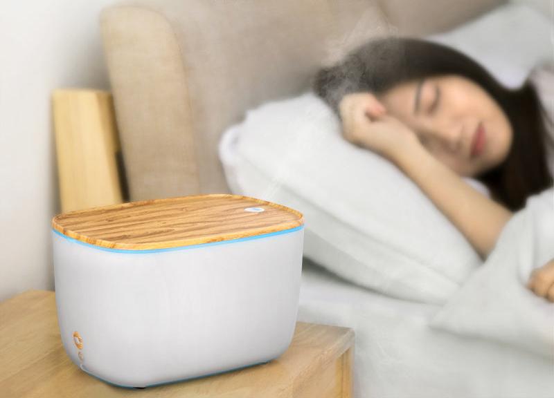 Moderner Luftbefeuchter aus Holz und Kunststoff im Schlafzimmer, Frau schläft im Hintergrund.