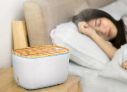 Moderner Luftbefeuchter aus Holz und Kunststoff im Schlafzimmer, Frau schläft im Hintergrund.